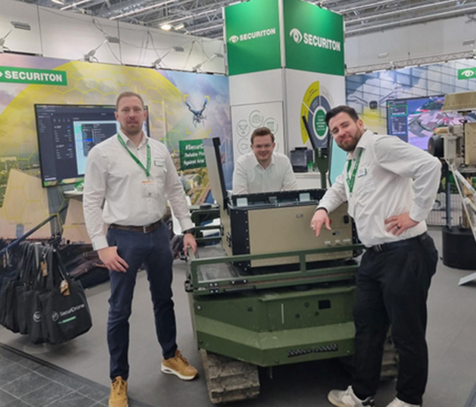 Das Securiton-Messe-Team, um Patrick Sielski, Henry Weinert und David Klumpp, steht neben einer Robotik-Sicherheitslösung von Securiton auf dem eigenen Messestand auf der Xponential Europe 2026.