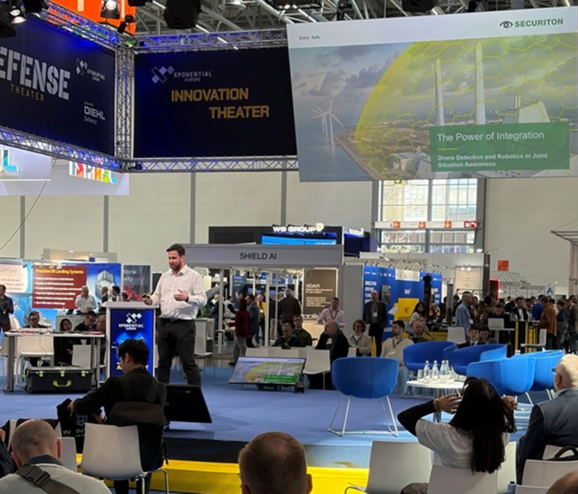 Henry Weinert, Teil des Securiton-Messe-Teams auf der Xponential Europe 2026, steht bei seinem Vortrag auf der Bühne. Im Hintergrund sieht man die Präsentationsfolie, auf der sich das Dome-Security-Konzept befindet.