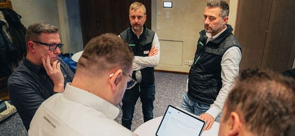 Ein Team von Securiton-Mitarbeitern (5 Männer),steht an einem Tisch und tauscht sich über ein Thema aus. Ein Kollege hält die Ergebnisse auf seinem Tablet fest.