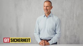 Im Mittelpunkt des Bildes steht Peter Treutler, Prokurist und Leiter der Business Unit IPS bei Securiton, an einem Tisch und vor einer grauen Wand. Links unten ist das "GIT Sicherheit"-Logo zu sehen.