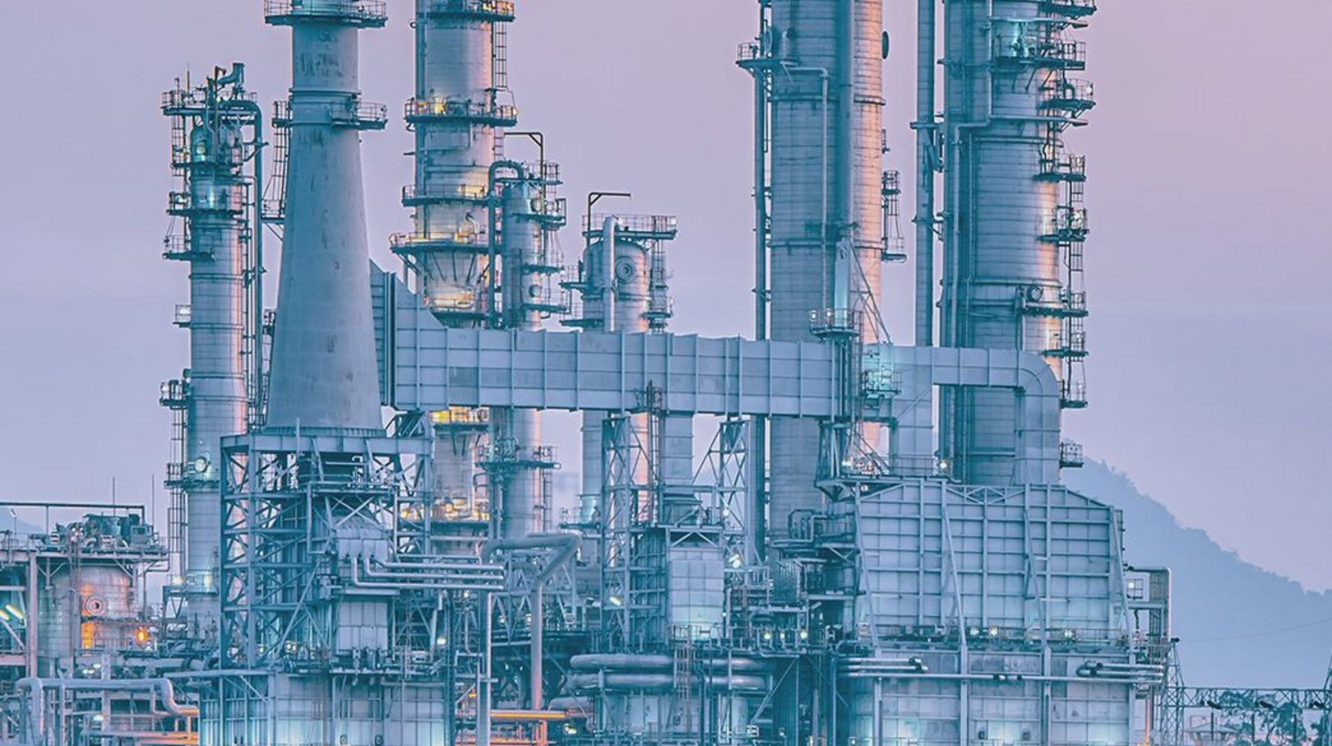 Detailansicht einer großen Industrieanlage mit mehreren hohen Türmen, Rohrleitungen und metallischen Strukturen. Die komplexe Anlage besteht aus dicht angeordneten technischen Aufbauten, Plattformen und Verrohrungen und wirkt wie ein petrochemisches oder energieerzeugendes Werk bei diffusem Tageslicht.