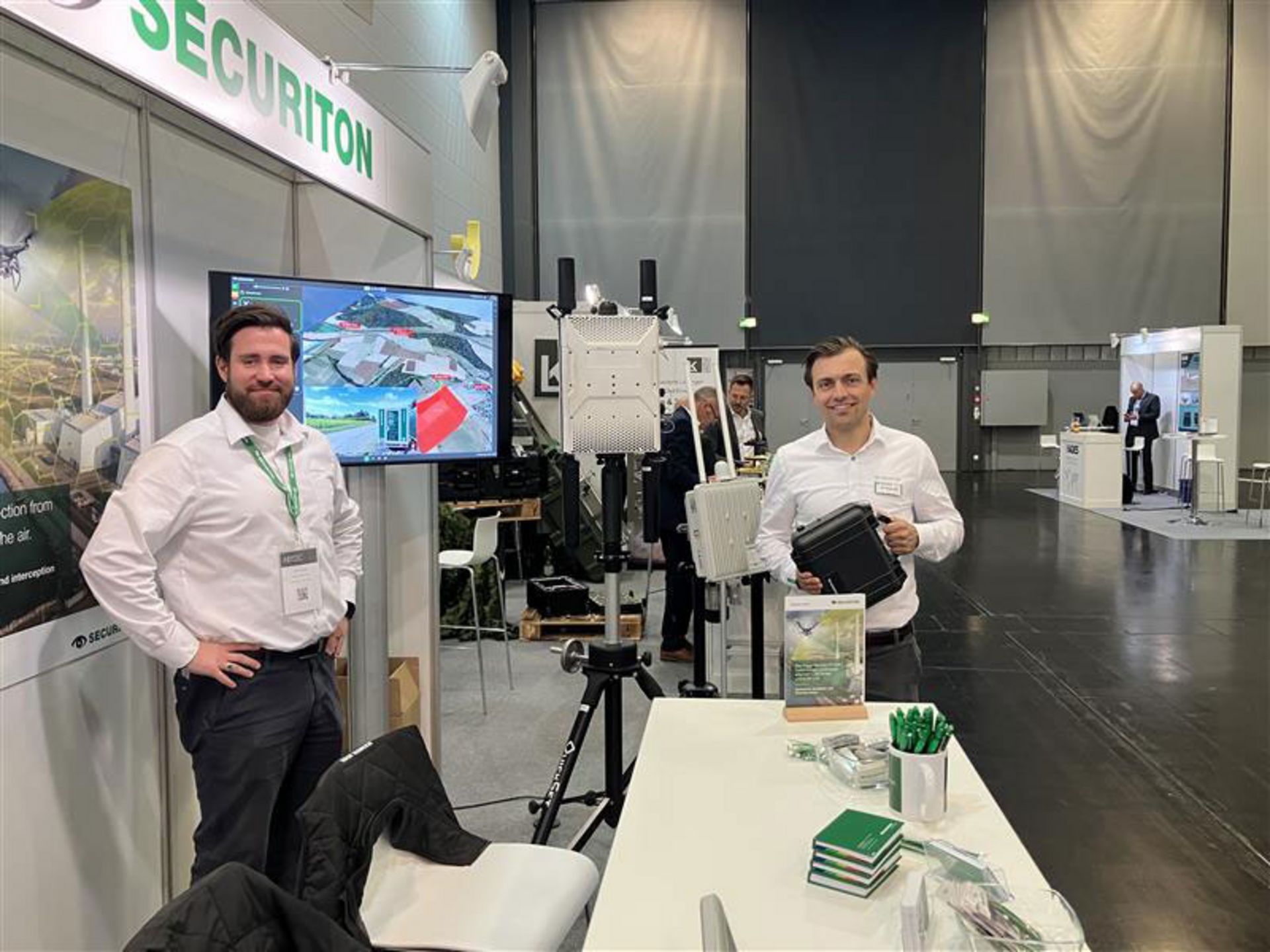 Zwei Mitarbeiter von Securiton, aus dem Bereich Sales Sicherheits-Speziallösungen, auf dem Securiton-Messestand der AIRTEC 2025 in Augsburg.