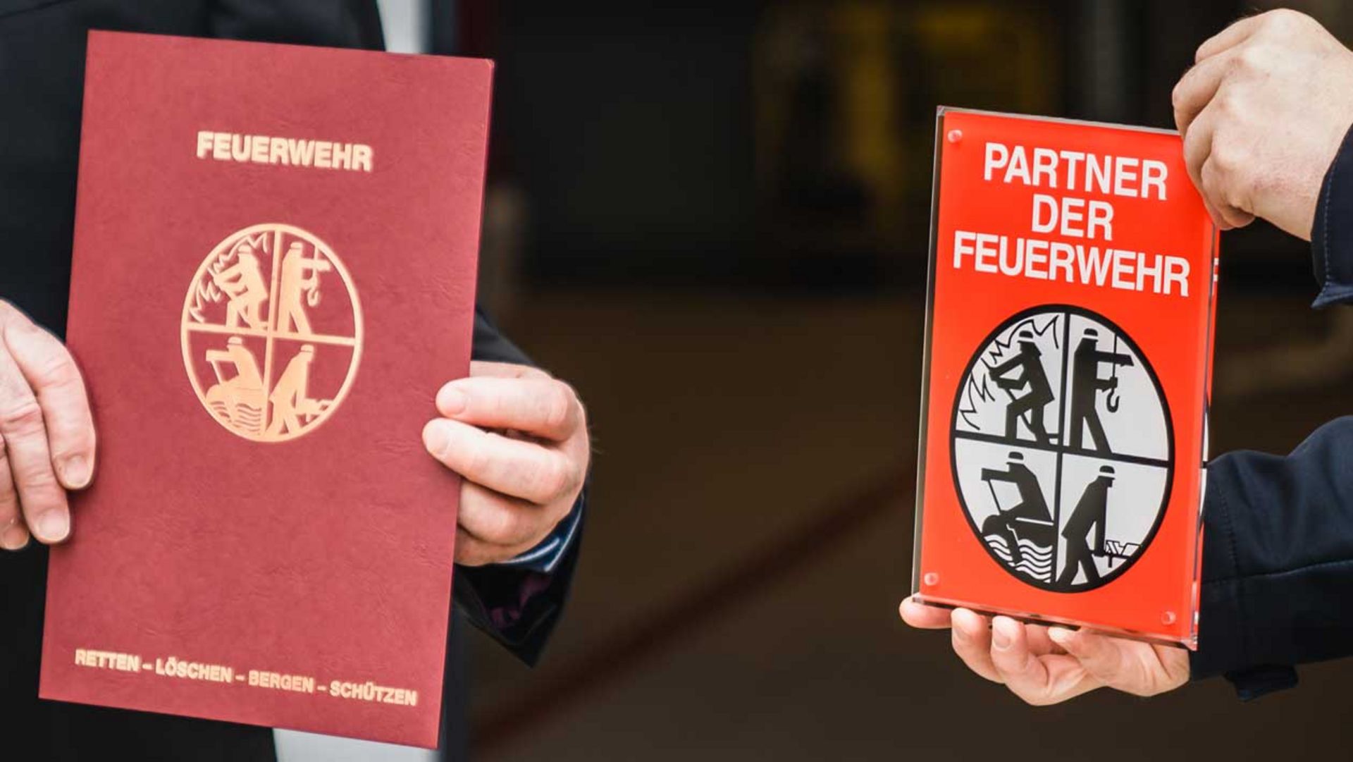 Es werden zwei Auszeichnungen in den Händen gehalten, eine die Auszeichnung als Partner der Feuerwehr.