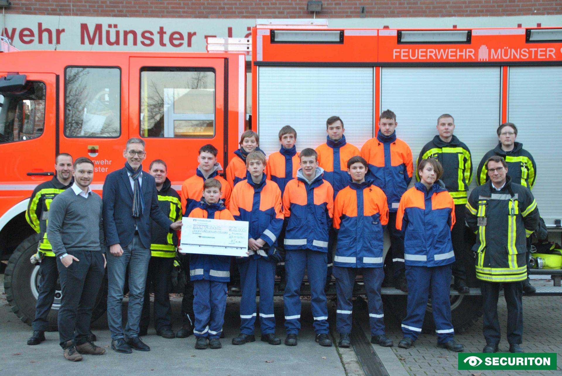 Die Übergabe des Spendenschecks vor einem Feuerwehrauto der Jugendfeuerwehr Münster. 