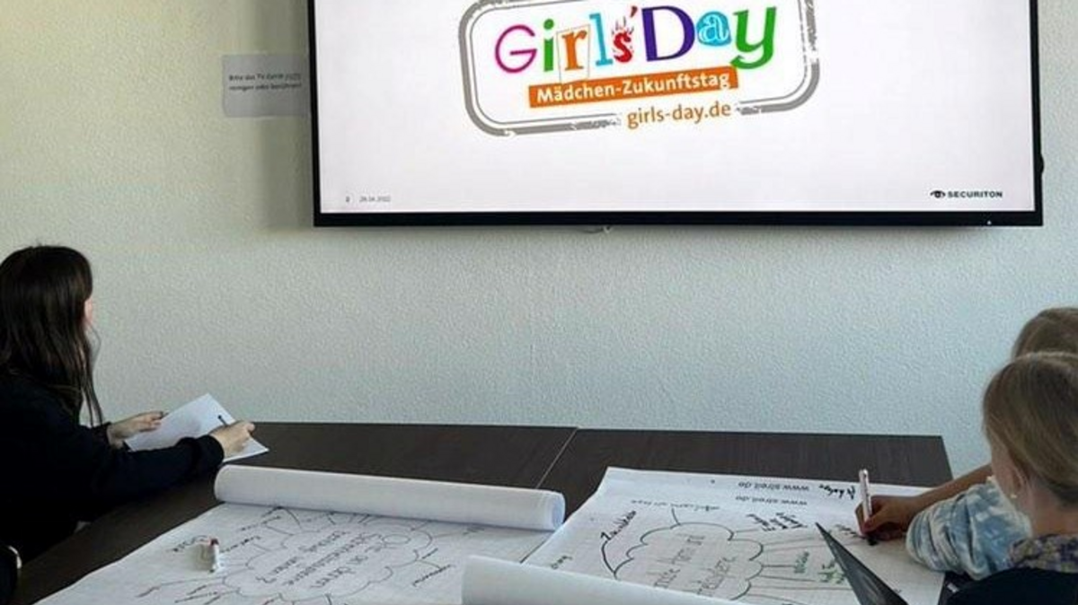 Drei Teilnehmerinnen des Securiton-Girls-Days schauen auf einen Bildschirm, auf dem eine PowerPoint geöffnet und das Girls Day Logo zu sehen ist. 