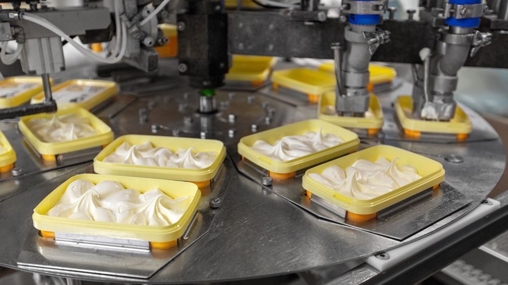 Automatisierte Produktionsanlage füllt cremige Lebensmittelmasse in Kunststoffbehälter ab, industrielle Abfüllmaschine in der Lebensmittelverarbeitung.